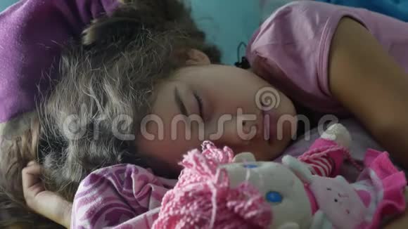 可爱的小女孩晚上睡在沙发床上拥抱她的婴儿室内娃娃少女黑发少女可爱的睡着了视频的预览图