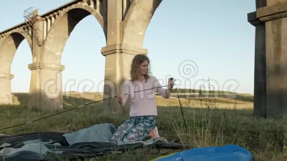 年轻女子在老桥附近收集一个旅游帐篷视频的预览图