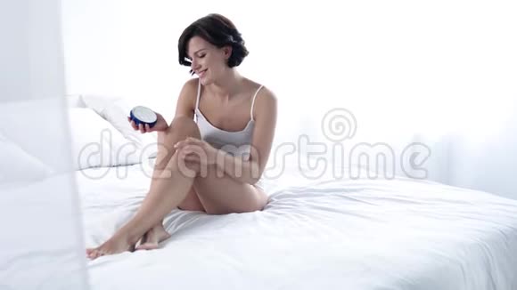 身体皮肤护理女性在卧室涂抹身体霜腿部皮肤视频的预览图