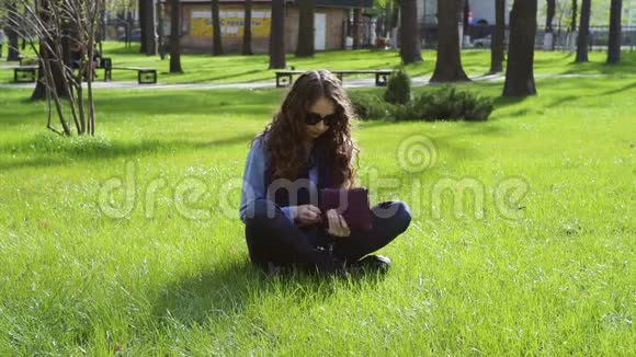 美丽的年轻女子坐在草地上的公园里看书视频的预览图