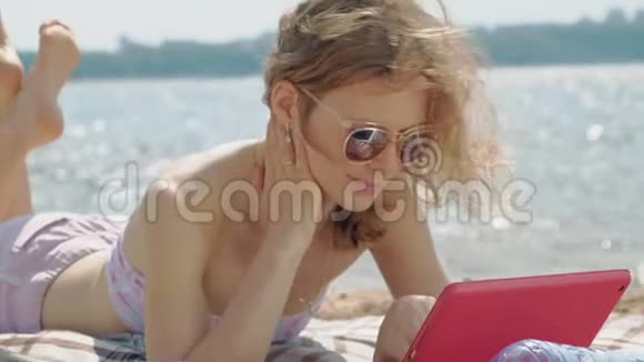 年轻女子在河岸的海滩上使用电脑平板电脑视频的预览图