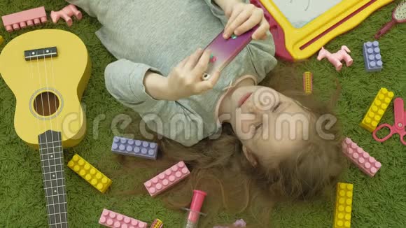 小女孩躺在绿色背景耳机和使用电话顶部视图视频的预览图