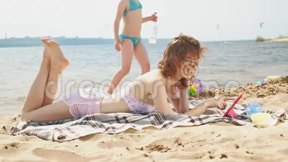 年轻女子在河岸的海滩上使用电脑平板电脑视频的预览图