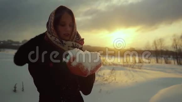 一位美丽的年轻女子在日落时吹着雪花慢慢地微笑着的冬天肖像1920x1080视频的预览图