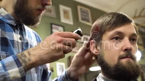 一个留胡子的理发师用梳子和修剪器仔细地给他的客户理发的肖像4K视频的预览图
