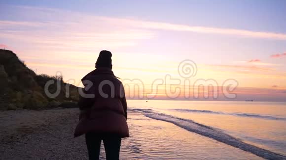 美丽的年轻女孩沿着海滩散步慢慢地走向美丽的日落视频的预览图