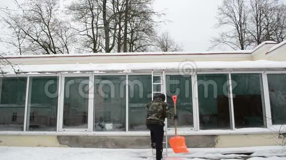 男人梯子橙色铲子干净的雪棚屋顶冬天视频的预览图