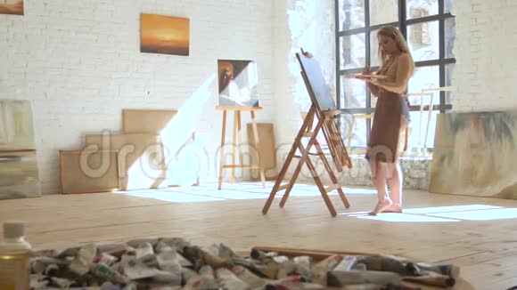 女艺术家在画架上的画布上作画并在艺术工作坊中担任调色板视频的预览图