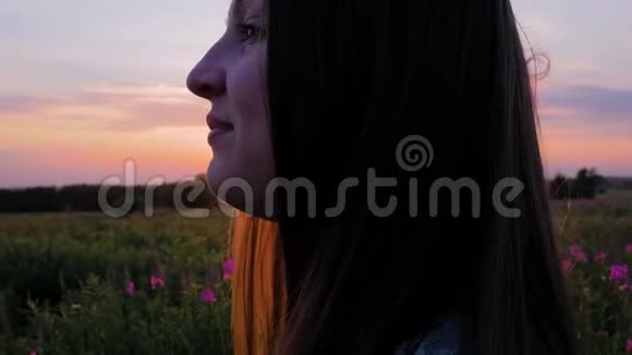 田野里年轻漂亮的女孩看着夕阳近距离射击视频的预览图
