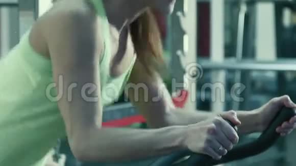 运动的女人在健身房骑着一辆静止的自行车在模拟器上踏板视频的预览图