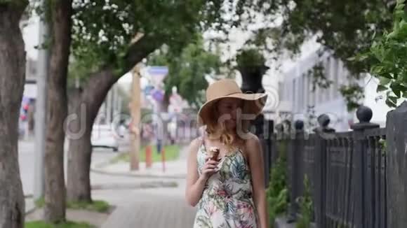 戴着帽子的漂亮年轻女人带着冰淇淋在城市里走来走去视频的预览图