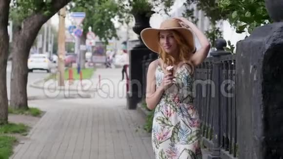 戴着帽子的漂亮年轻女人带着冰淇淋在城市里走来走去视频的预览图