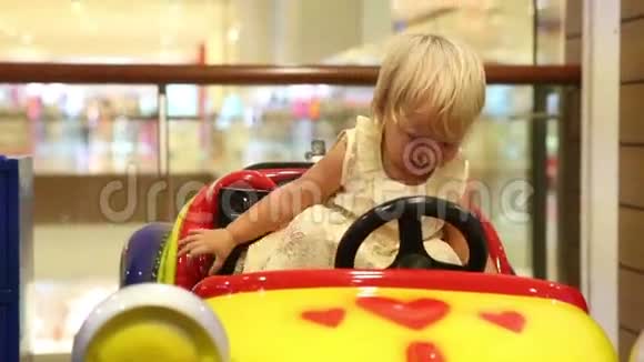 一个金发小男孩坐在玩具车里开心视频的预览图