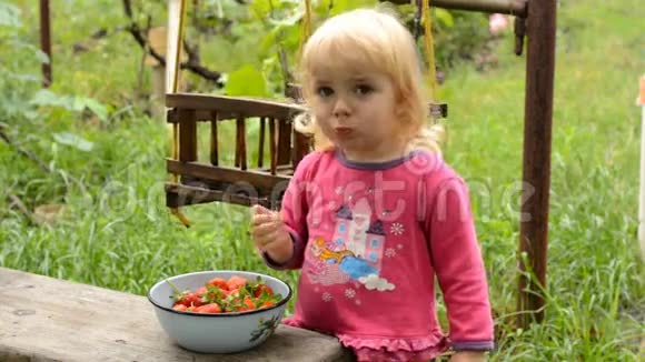 可爱的小女孩在绿色花园吃草莓视频的预览图