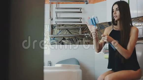 有魅力的女孩坐在浴室里的厕所里带着蓝色的monopod自拍视频的预览图