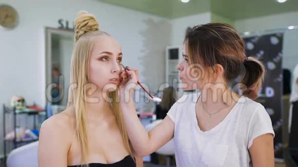 转型在时髦的美容院一位专业的化妆师为一位迷人的金发女郎准备形象视频的预览图