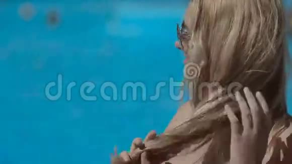 穿着比基尼的金发女郎坐在游泳池附近视频的预览图