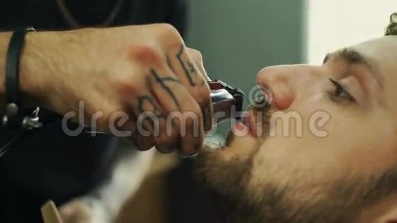 有才华的留胡子的理发师正在理发店里用黑色的剪发披风修剪他的客户的胡须他用的是视频的预览图
