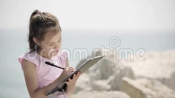 一个孩子坐在亚得里亚海附近的一块石头上画画视频的预览图