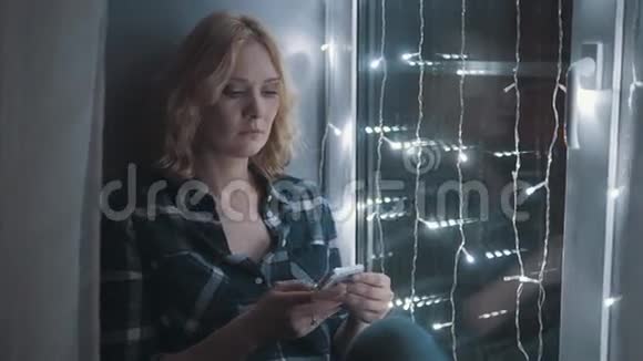 美丽迷人的女人使用智能手机坐在窗前装饰着花环视频的预览图