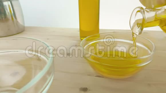 在靠近橄榄油瓶的木桌背景上的白色容器中倒入食用油慢镜头拍摄视频的预览图