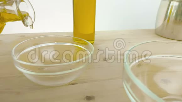 在靠近橄榄油瓶的木桌背景上的白色容器中倒入食用油慢镜头拍摄视频的预览图