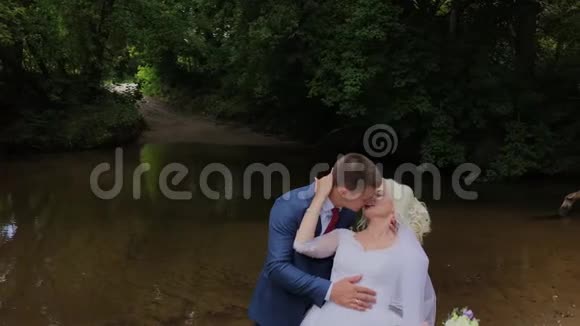 美丽的新郎和金发新娘在森林里的小溪旁视频的预览图