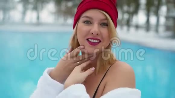 年轻的金发女郎穿着浴袍在冬天的室外游泳池附近有一间红色的小屋视频的预览图
