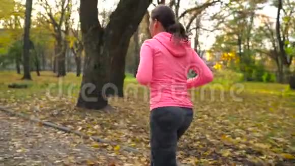 日落时分一位戴着耳机和智能手机的女士在秋天的公园里奔跑慢动作视频的预览图