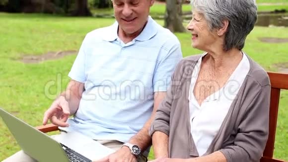 退休夫妇坐在公园长椅上用笔记本电脑视频的预览图
