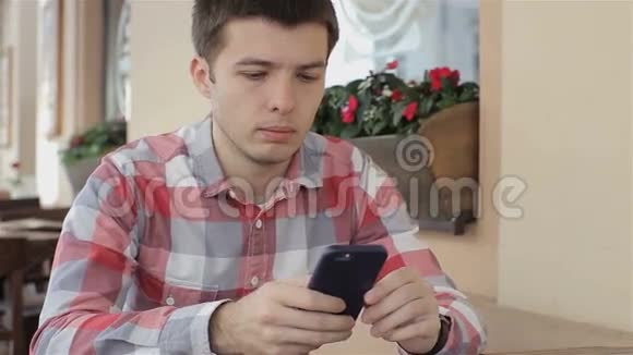 年轻人在咖啡馆里用智能手机发短信年轻人用他的智能手机从互联网上购买商品视频的预览图