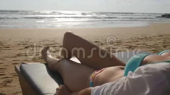 年轻女子躺在海边的日光浴床上晒黑女性身体在躺椅上放松和享受夏天视频的预览图