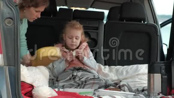 美丽的小女孩坐在一辆敞篷的汽车后备箱里在河岸上玩黄色的四弦琴视频的预览图