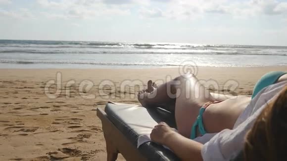年轻女子躺在海边的日光浴床上晒黑女性身体在躺椅上放松和享受夏天视频的预览图