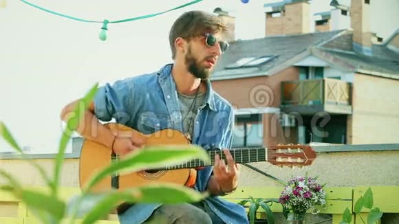 阳光明媚的一天英俊的音乐家在屋顶聚会上弹吉他视频的预览图