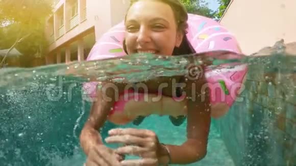 年轻时髦的千禧女孩穿着洒满甜甜圈漂浮在游泳池微笑着看着相机年轻快乐的女人放松视频的预览图