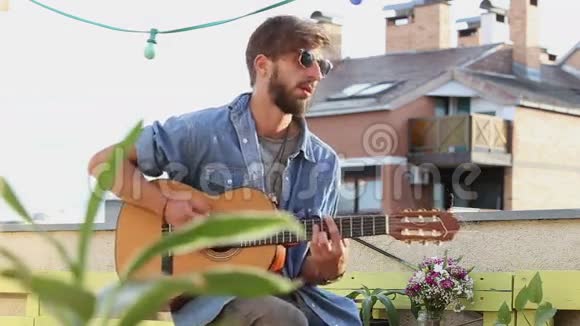 阳光明媚的一天英俊的音乐家在屋顶聚会上弹吉他视频的预览图
