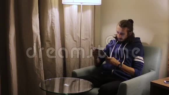 帅哥有平板电脑的年轻人坐在家里的椅子上视频的预览图