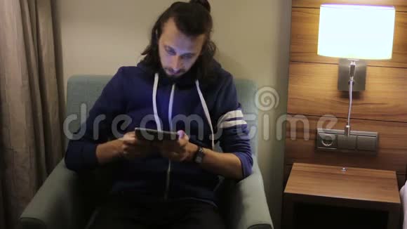 帅哥有平板电脑的年轻人坐在家里的椅子上视频的预览图