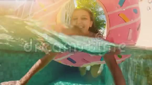 阳光明媚的夏日戴着蓝色比基尼太阳镜的女人躺在充气的粉红色甜甜圈里漂浮在游泳池里看镜头视频的预览图