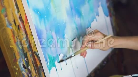 年轻的女画家用水彩画和画笔在画架画布上画特写视频的预览图