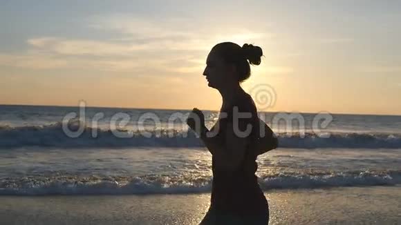 日落时在海边奔跑的年轻女子剪影日出时沿着海岸慢跑的女孩女性视频的预览图