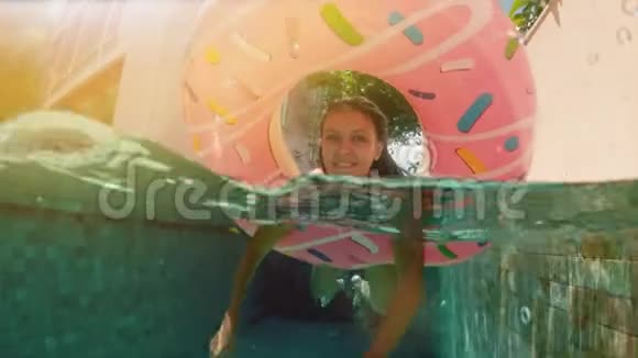 年轻时髦的千禧女孩穿着洒满甜甜圈漂浮在游泳池微笑着看着相机年轻快乐的女人放松视频的预览图