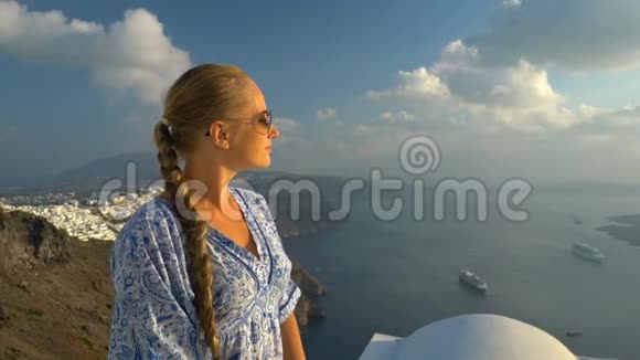 快乐的女人穿着白色和蓝色的裙子在希腊的桑托里尼享受她的假期从卡尔德拉和爱琴海观景视频的预览图