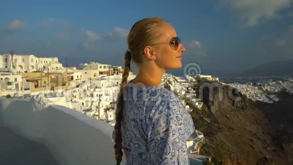 快乐的女人穿着白色和蓝色的裙子在希腊的桑托里尼享受她的假期从卡尔德拉和爱琴海观景视频的预览图