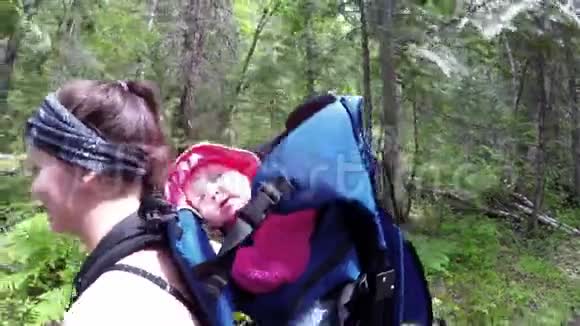 母亲背着婴儿背着背包穿过森林4k视频的预览图