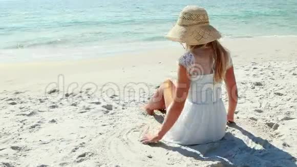 金发女人坐在海滩上看海洋的后景视频的预览图