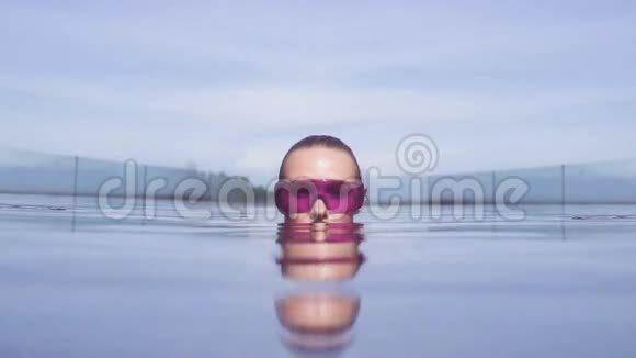 在阳光明媚的一天年轻女子戴着紫色太阳镜在无限屋顶游泳池里看相机视频的预览图