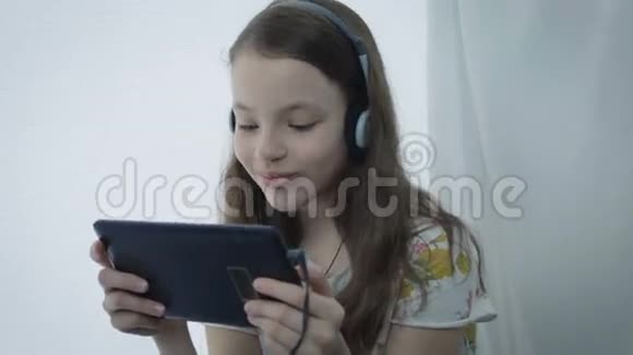 带着耳机看平板电脑上的搞笑视频的漂亮小女孩视频的预览图