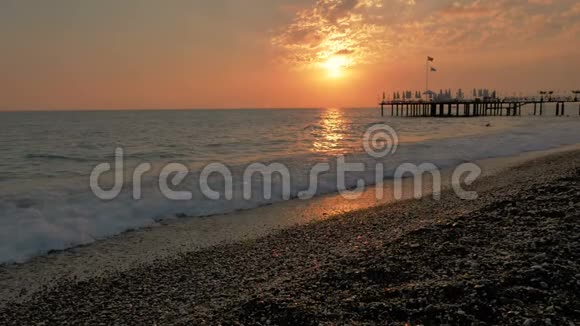 五彩缤纷的日落海浪和泡沫的海景码头和卵石海滩视频的预览图